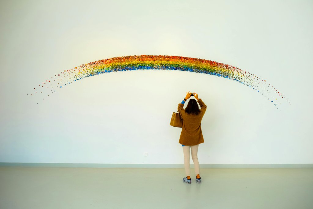 Woman Wearing Brown Top and Beige Leggings Taking Picture Rainbow Painted Wall