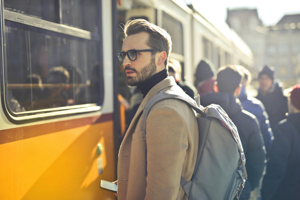 Man in Brown Coat and Gray Backpack Posing for a Photo