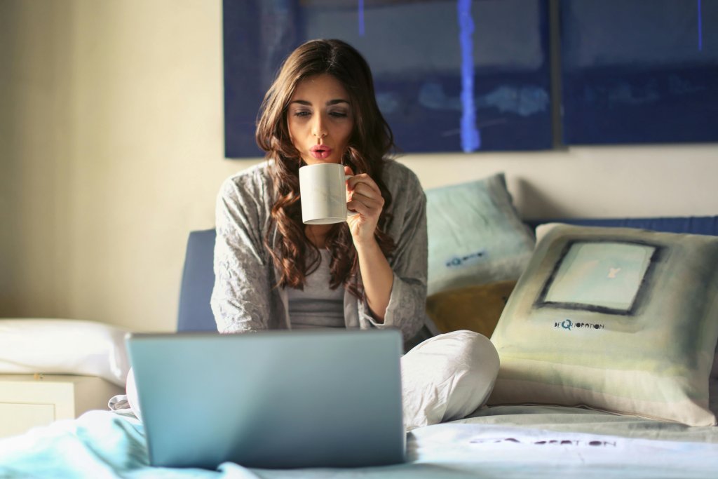 Woman in Grey Jacket Sits on Bed Uses Grey Laptop